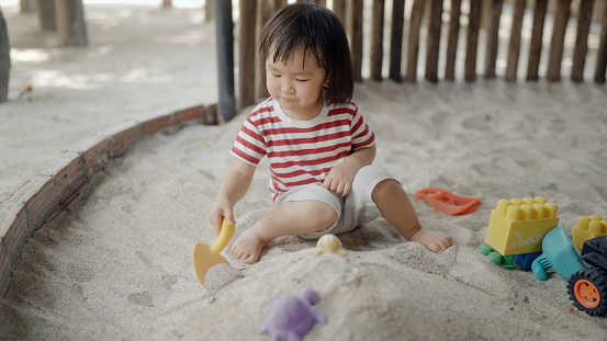 Little girl builds a pile of sand in a sand pit