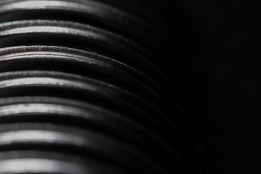 Close up of the thread of a metallic screw on black background, textured metal, abstract macro