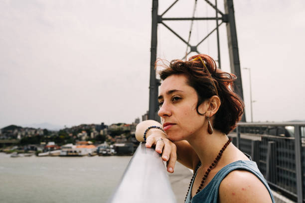 Young woman leaning on the railing of a bridge and looking out at the scenic view of a river