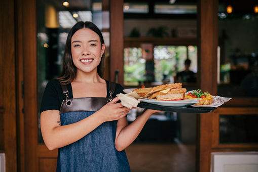 Smiling waitress standing and holding tray of food in a restaurant and looking at camera