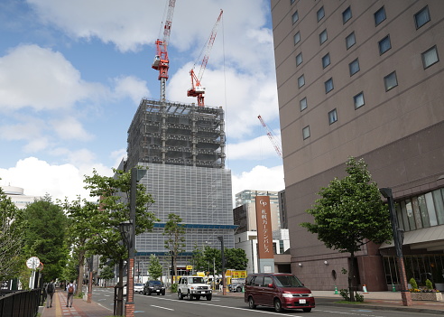 Sapporo, Japan - May 30, 2023: Three construction cranes on different sites in downtown. Street level view on Kita Jonishi outside the Sapporo Grand Hotel. Spring afternoon with light clouds in Hokkaido Prefecture.