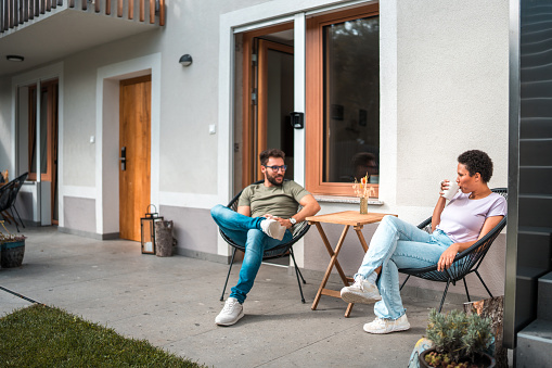 Amidst a countryside escape, a mid-adult multicultural couple relishes a relaxing vacation in an outdoor setting, sharing quality time and engaging in conversation while dressed in casual attire.
