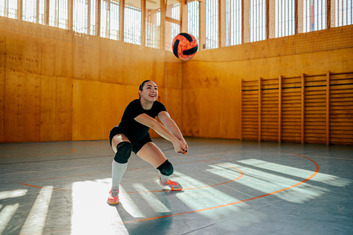 A female teenage professional volleyball player is hitting and passing a ball on indoor court on training.A young sportswoman in action hitting and passing the ball on volleyball court during training