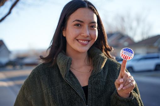 Young Hispanic Woman in Her Twenties Holding an I Voted Sticker Smiling at the Camera Shallow Depth of Field