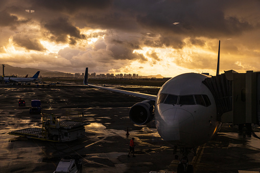 Silhouetted fuselage of aircraft docked at gate with airport atmosphere at sunrise. Shot in Hawaii.