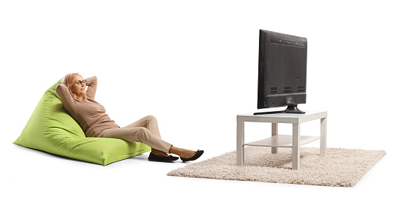 Middle aged woman on a green bean bag armchair watching tv isolated on white background