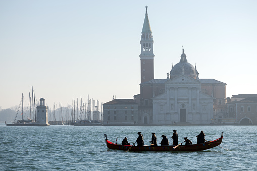Venezia, Veneto, Italy - January 28, 2024: Venetian Gondola with Historical Traditional Venetian Masks on it Navigating Beside the Church of San Giorgio Maggiore