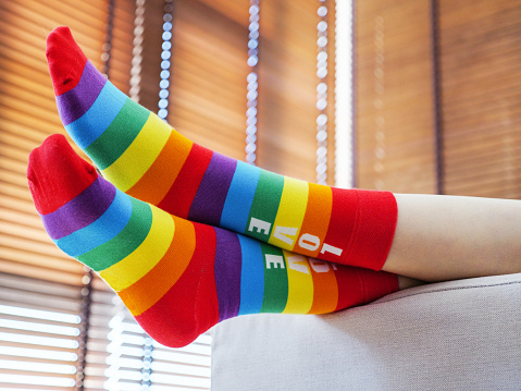 Woman wearing rainbow socks lying on the sofa at home. Rainbow stripes as a modern sign of the LGBT community