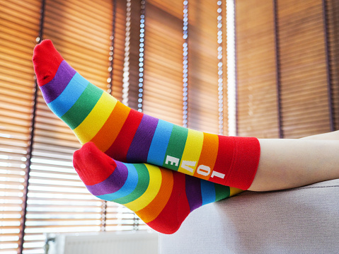 Woman wearing rainbow socks lying on the sofa at home. Rainbow stripes as a modern sign of the LGBT community