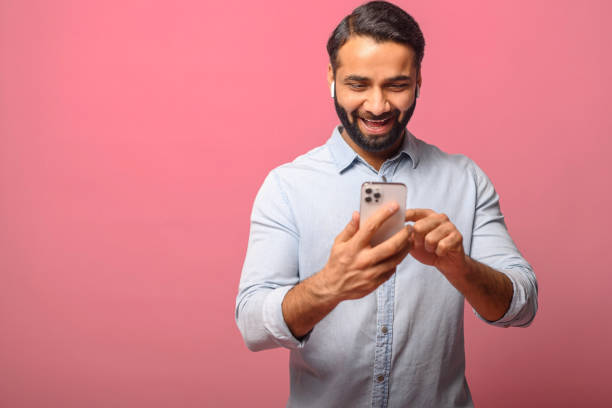istock Smiling Indian man holding and using smartphone, carefree multiracial guy enjoying online chatting 1991376410