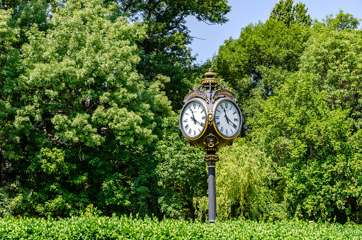 Vintage style black and gold metallic clock at the entry in Cismigiu Park, in Bucharest, Romania, in a sunny summer day