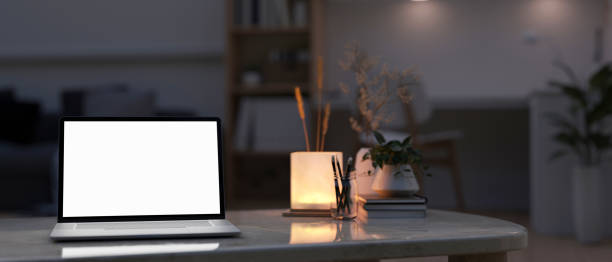 istock A laptop mockup, a table lamp, and accessories on a coffee table in a modern room at night. 1991448803