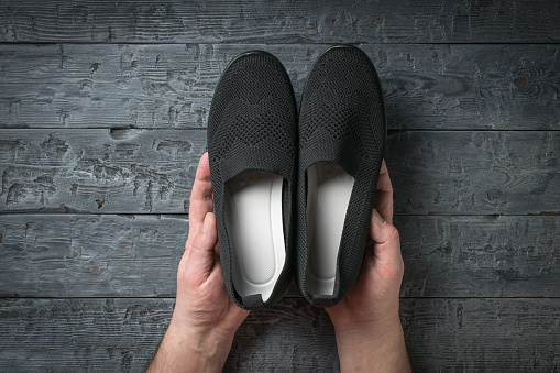 A man holds rag black women's shoes on a wooden background. Casual shoes.