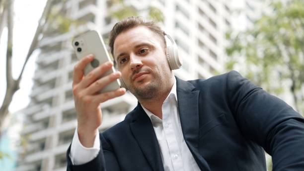 inteligentni biznesmeni noszą słuchawki, patrząc na telefon w zielonym mieście. miejski. - office park audio zdjęcia i obrazy z banku zdjęć