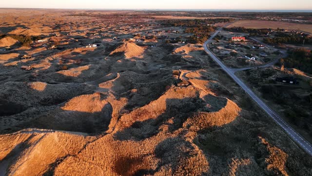 Aerial view Houses are built between the sand dunes, and the dunes are illuminated by the yellow color of the sunset.