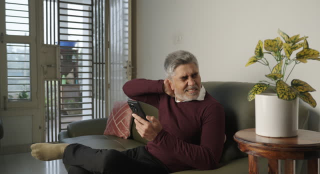Old man touching neck in pain on sofa