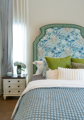 Interior view of luxury decorated green and blue headboard bedroom with side table lamp.