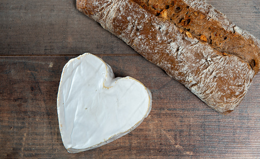 a French Neufchatel cheese shaped heart with bread on wooden background