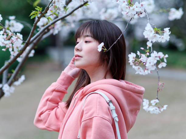 istock Beautiful young Chinese woman posing under blooming cherry tree, wearing pink loose oversized top with small white shoulder bag. Candid moment. Emotions, people, beauty, youth and lifestyle portrait. 1991799609