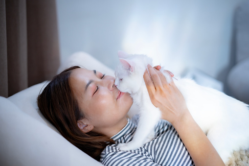 Young Asian woman kissing with her white kitten with happy moment for cat lover, with love and adorable relationship and interact with pet and owner at home, woman with pet lifestyle, healling, comfortable mind at home.
