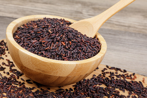 A Wooden Bowl of delicious and healthy Black Rice isolated on a wooden background with copy space