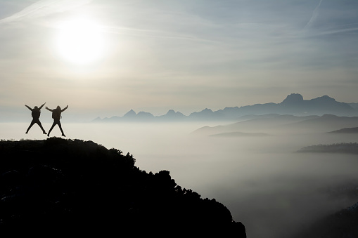 Successful people at sunrise on top of misty mountains