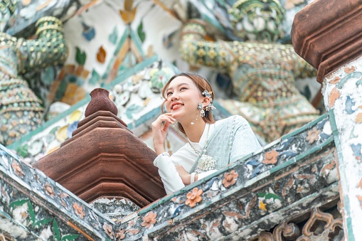 Young Asian woman exudes elegance and cultural pride in a stunning traditional Thai costume at the Temple of Dawn - Wat Arun.