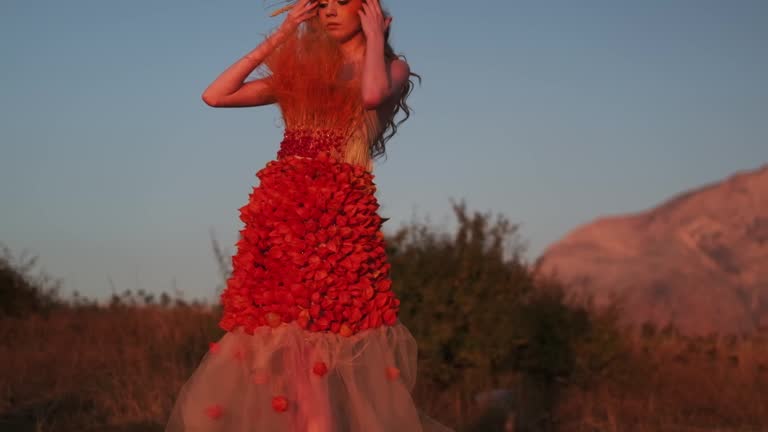 A young woman in an autumn outfit of flowers and grass and a headdress made of ears of corn stands against the background of the sunset in the mountains