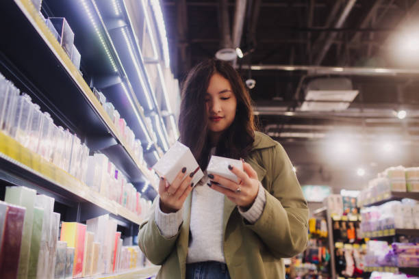 menina que faz compras na loja de varejo. bela adolescente testando e comprando cosméticos em uma loja de beleza. vista lateral. cuidados pessoais e cosmetologia moderna. beleza e moda. varejo e consumismo. - asian ethnicity women shopping mall perfume - fotografias e filmes do acervo