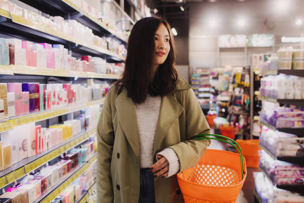 young girl shopping in retail store. beautiful teenage testing and buying cosmetics in a beauty store. side view. personal care and modern cosmetology. beauty and fashion. retail and consumerism. - asian ethnicity women shopping mall perfume photos et images de collection