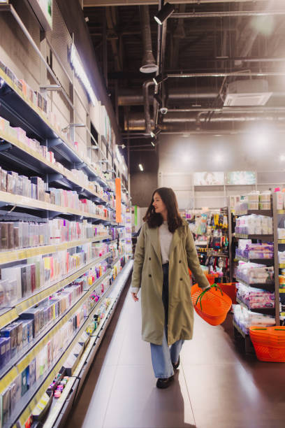 young girl shopping in retail store. beautiful teenage testing and buying cosmetics in a beauty store. side view. personal care and modern cosmetology. beauty and fashion. retail and consumerism. - asian ethnicity women shopping mall perfume ストックフォトと画像