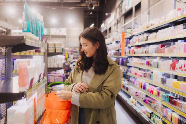 jeune fille faisant du shopping dans un magasin de détail. belle adolescente testant et achetant des cosmétiques dans un magasin de beauté. vue latérale. soins personnels et cosmétologie moderne. beauté et mode. commerce de détail et consumérisme. - asian ethnicity women shopping mall perfume photos et images de collection