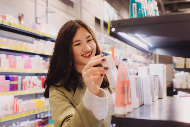 menina segura uma garrafa de creme em suas mãos em loja de varejo. mulher bonita testando e comprando cosméticos em uma loja de beleza. vista lateral. cuidados pessoais e cosmetologia moderna. - asian ethnicity women shopping mall perfume - fotografias e filmes do acervo