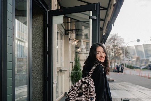 Portrait of cute Korean girl holding a gift box and drinking coffee in cafe near window. Teenage girl walking through the city and having fun. Travel, vacation and holiday concept