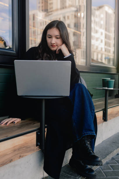 portrait d’une jolie fille coréenne dans un café près de la fenêtre et du réseautage, regardant un ordinateur portable et buvant du café. étudiant prenant un cappuccino et travaillant sur des ordinateurs portables à l’extérieur. le plaisir de  - red text messaging cafe teenage girls photos et images de collection