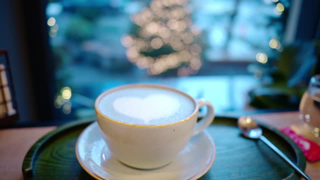 Cup of coffee with foam latte art in heart shape. Christmas tree on background