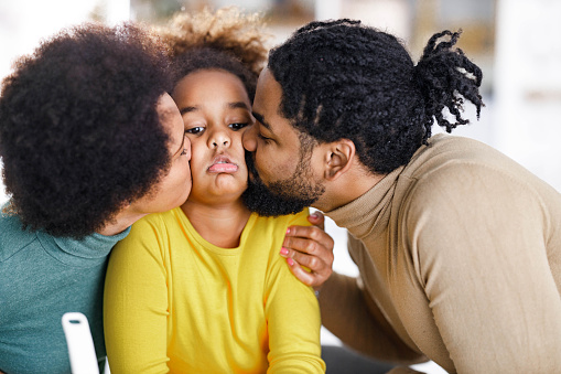 African American girl being kissed by her parents at home.