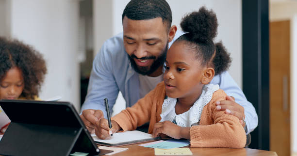 istock Father, kids and book for writing, tablet and teaching with support for education, development or studying at desk. Dad, children and help with homework, online course and home school in family house 1991952404