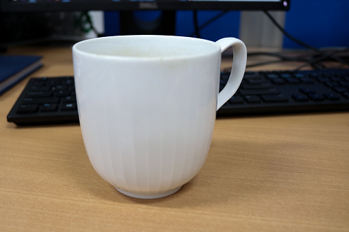 Photo of a white mug with hot chocolate, the mug is on the office desk in the morning
