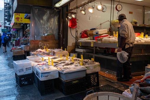 New York, NY, USA 11-09-2023 Pedestrians in background at NYC Chinatown Asian food market bins of seafood fish shrimp and ingredients on ice with hand written price cards and one worker. Busy colorful city street. Editorial use only.