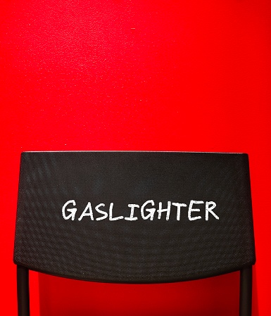 Chair back on red copy space wall with text written GASLIGHTER, abuser who tries to control victim by twisting their sense of reality - manipulation in abusive relationships