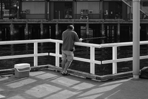 Sydney, Australia - February 04, 2024: Sunny morning in Walsh bay in Sydney, a man fishing on a pier.