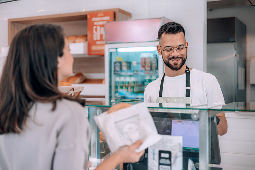 With a sense of ease, a customer completes her bakery purchase using a credit card, facilitated by the attentive male worker