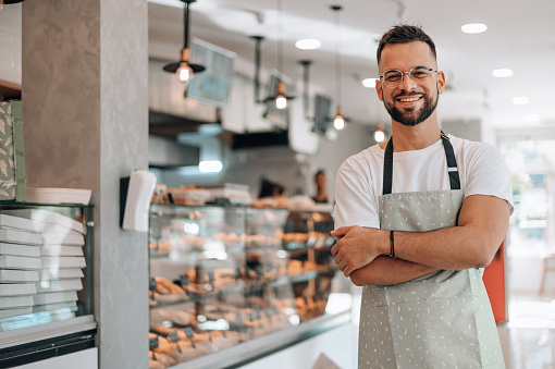 A skilled male bakery worker takes a moment to pose for the camera, showcasing his dedication and craftsmanship in the bakery
