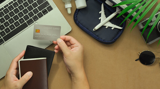 Top view of woman hand holding credit card with travel accessories and passport on desk. Traveling concepts.