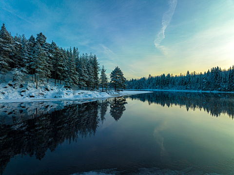 A serene lake surrounded by snow-covered trees against the backdrop of the blue sky