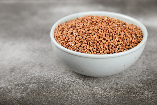 Raw buckwheat in a bowl on a textured background.Wheat grains, porridge, cereals, raw buckwheat in a plate. Healthy food. Porridge. Diet. Organic cerea. Space for text.Copy space.