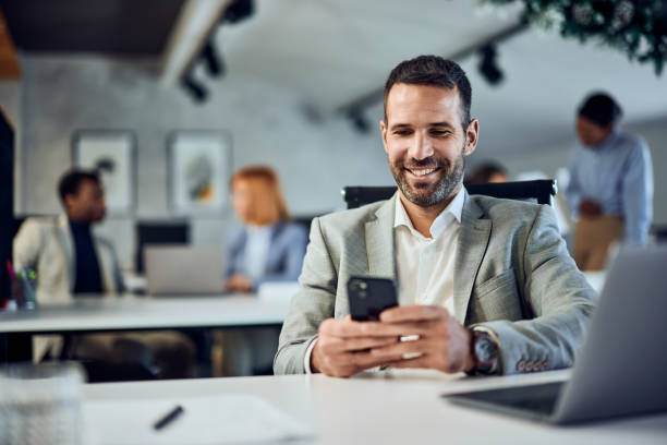 istock A smiling businessman using a mobile phone in the co-working space, colleagues in the background. 1992064056