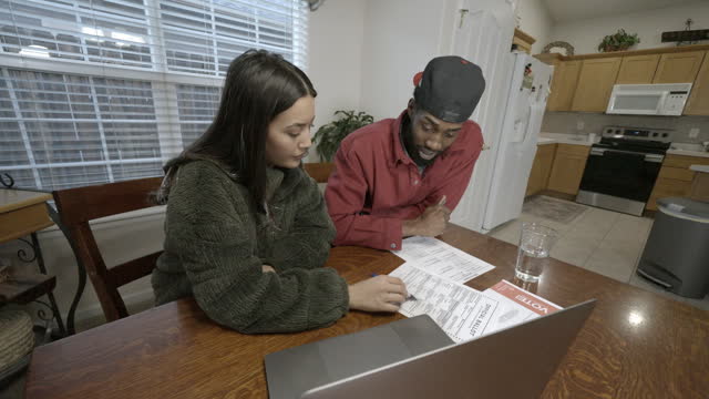 Young Mixed Race Couple Hispanic and African American Sitting at a Kitchen Table Researching Issues and Candidates and Filling Out a Mail In Voting Ballot