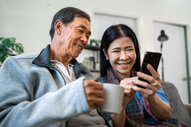 istock Retired elderly couple sits on couch drink tea and using mobile together and relax in their home. Senior Activity Concept 1992079105